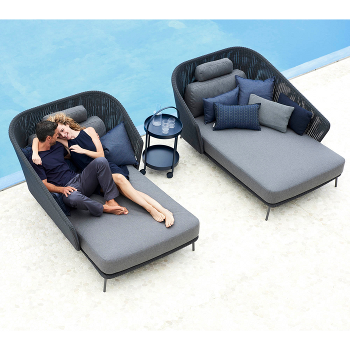 lifestyle image of cane-line mega right daybed in Graphite, Small Round Cane-line Weave Incl. Grey Cane-line AirTouch in a patio with outdoor furniture and two people enjoying the daybed