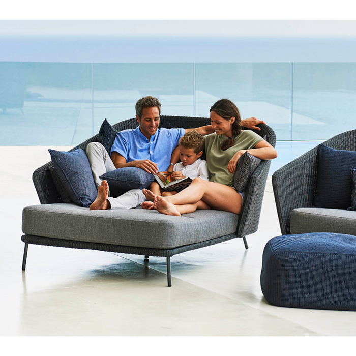 lifestyle image of cane-line mega right daybed in Graphite, Small Round Cane-line Weave Incl. Grey Cane-line AirTouch in a patio with outdoor furniture and a family enjoying the daybed