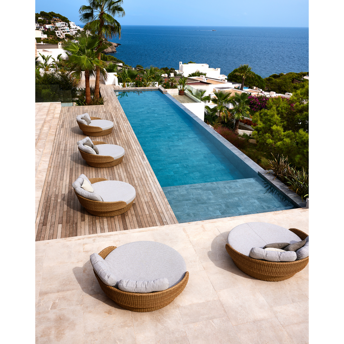 lifestyle image of cane-line ocean large daybed in Natural, Large Flat Cane-line Weave daybed with Light Brown, Cane-line Wove cushion with outdoor cushions in a patio with pool