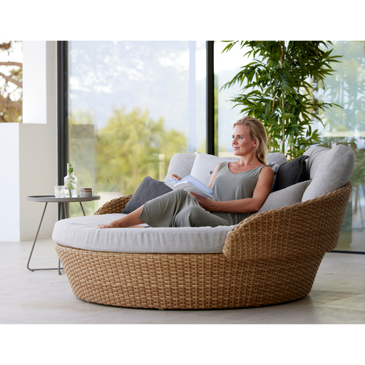 lifestyle image of cane-line ocean large daybed in Natural, Large Flat Cane-line Weave daybed with Light Brown, Cane-line Wove cushion in a patio with a woman enjoying the daybed