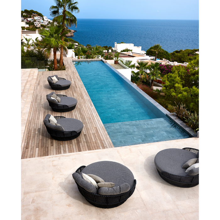 lifestyle image of cane-line ocean large daybed in Dark Grey, Open Cane-line Soft Rope daybed with Light Brown, Cane-line Wove cushion with outdoor cushions in a patio with pool