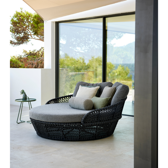 lifestyle image of cane-line ocean large daybed in Dark Grey, Open Cane-line Soft Rope daybed with Light Brown, Cane-line Wove cushion with outdoor cushions in a patio
