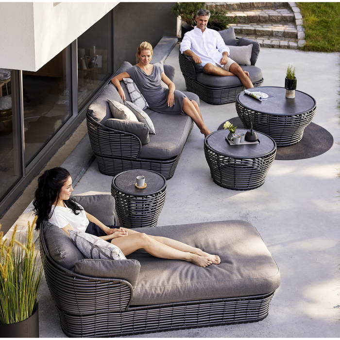 lifestyle image of cane-line basket daybed in Graphite, Braid Cane-line Weave w/Grey Cane-line AirTouch in a patio with basket furniture and a woman enjoying the daybed