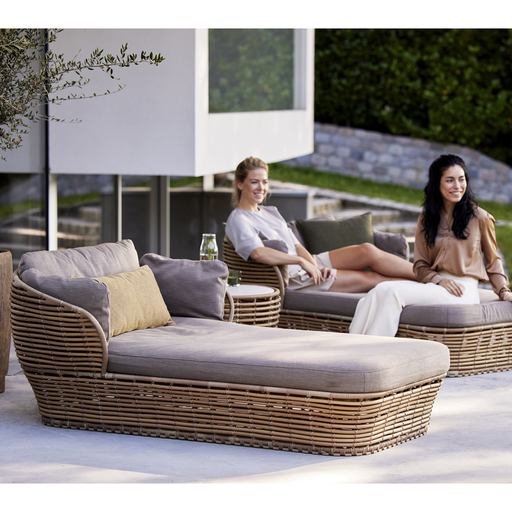lifestyle image of cane-line basket daybed in Natural, Braid Cane-line Weave Incl. Taupe Cane-line AirTouch in a patio with outdoor furniture and two women enjoying a daybed