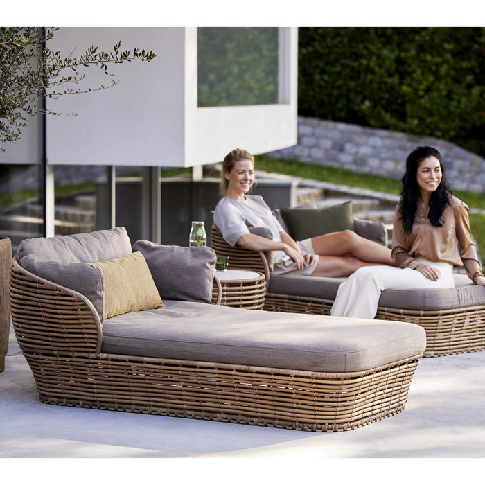 lifestyle image of cane-line basket daybed in Natural, Braid Cane-line Weave Incl. Taupe Cane-line AirTouch in a patio with outdoor furniture and two women enjoying a daybed