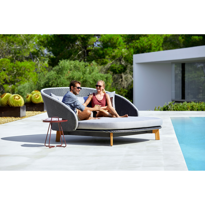 cane-line peacock daybed without parasol in a pool with 2 people enjoying the daybed
