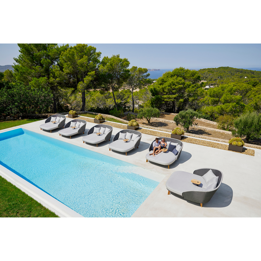 cane-line peacock daybed without parasol in a pool with all the peacock daybeds and 2 people enjoying the daybed