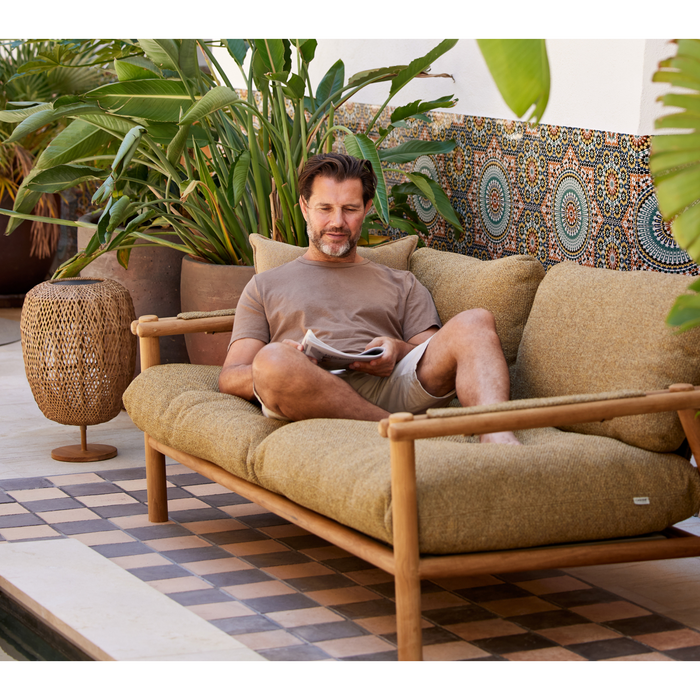 sticks 2 seater sofa Teak sofa turmeric yellow Cane-line Rise cushion with a man enjoying the sofa lifestyle