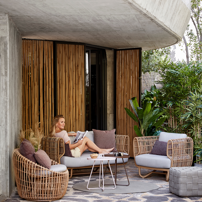 Nest outdoor 2 seater Sofa Light Grey Natte cushion in patio with outdoor furniture and a woman enjoying the sofa lifestyle