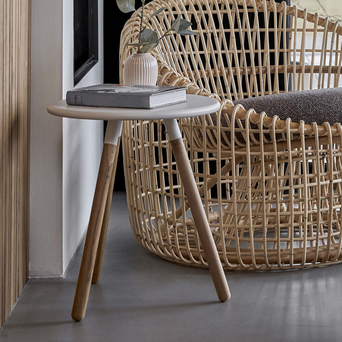 lifestyle image of cane-line area table stool in Teak w/White Aluminium in a room with nest chair