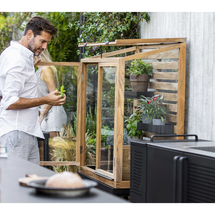 lifestyle image of cane-line drop greenhouse in Teak w/Lava Grey Aluminium in a garden with plants inside