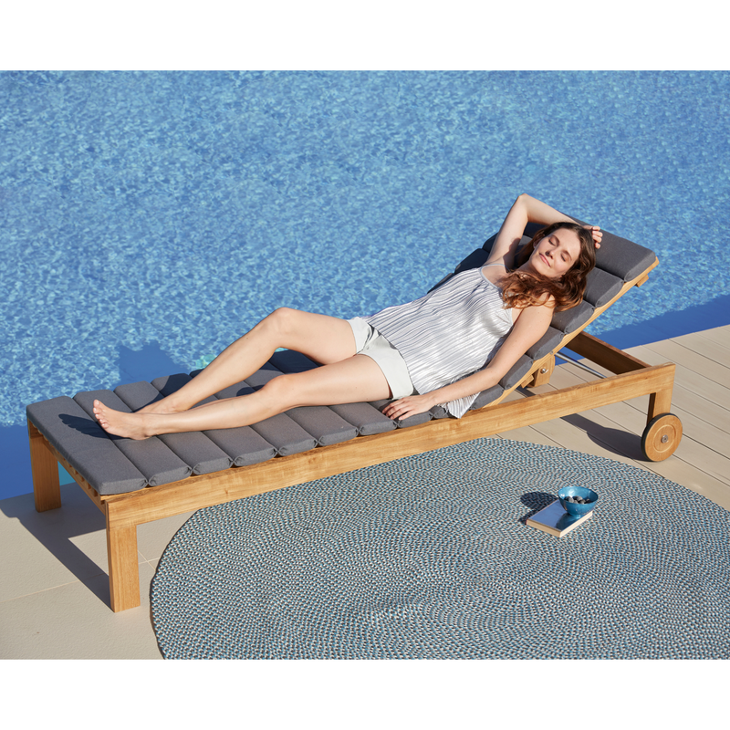 cane-line amaze sunbed teak sunbed with grey, cane-line natté cushion leaning forward with carpet an a woman enjoying the sunbed in a pool lifestyle