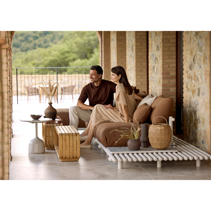 cane-line mellow sofa module coffee table teak coffee table with outdoor furniture, sticks platform sofa and two people enjoying the sofa lifestyle