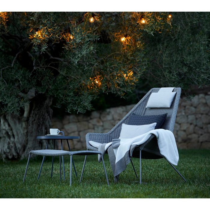 lifestyle image of cane-line breeze footstool in Light Grey, Small Round Cane-line Weave with outdoor chair and coffee table in a garden