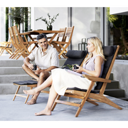 cane-line flip deck chair teak chair with Dark grey, Cane-line Focus cushion in a patio with two people enjoying the chair lifestyle 