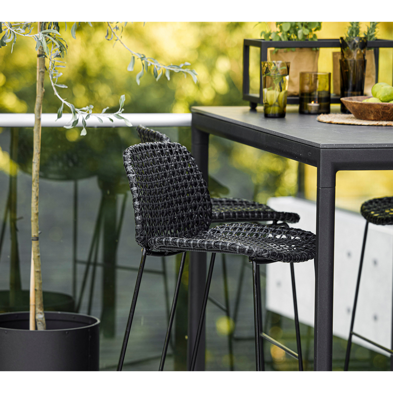 lifestyle image of cane-line vibe bar chair in Black/Graphite, Small Cross Cane-line Weave in a patio with bar table