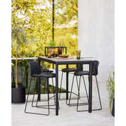 lifestyle image of cane-line vibe bar chair in Black/Graphite, Small Cross Cane-line Weave in a patio with bar table