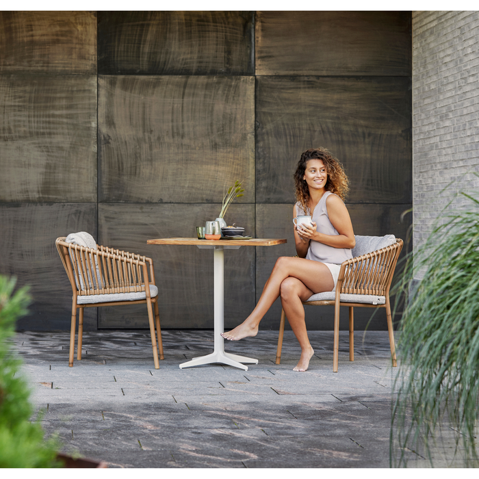 cane-line ocean chair Natural, Medium Round Tube Cane-line Weave chair with Light Brown, Cane-line Rise cushion in a patio with table and a woman enjoying the chair lifestyle