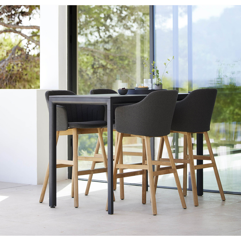 lifestyle image of cane-line choice bar chair in Black, Polypropylene, Up to 98% Recycled chair, teak base and Black, Cane-line Natté cushion with bar table in a patio