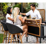 lifestyle image of cane-line peacock bar chair in Dark Grey, Medium Flat Cane-line Soft Rope w/Teak chair with Dark Grey, Cane-line Focus cushion in a patio with two women enjoying the chair