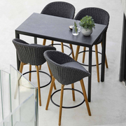 lifestyle image of cane-line peacock bar chair in Dark Grey, Medium Flat Cane-line Soft Rope w/Teak chair with Grey, Cane-line Natté cushion in a patio with bar table