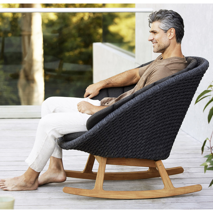 cane-line peacock rocking chair Dark Grey, Medium Flat Cane-line Soft Rope with Teak and Dark Grey, Cane-line Focus cushion in a patio with a man enjoying the chair lifestyle