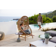 cane line hive chair Natural, small round tube Cane-line Weave with teak base and Taupe, Cane-line AirTouch cushion in a patio with a woman enjoying the chair lifestyle