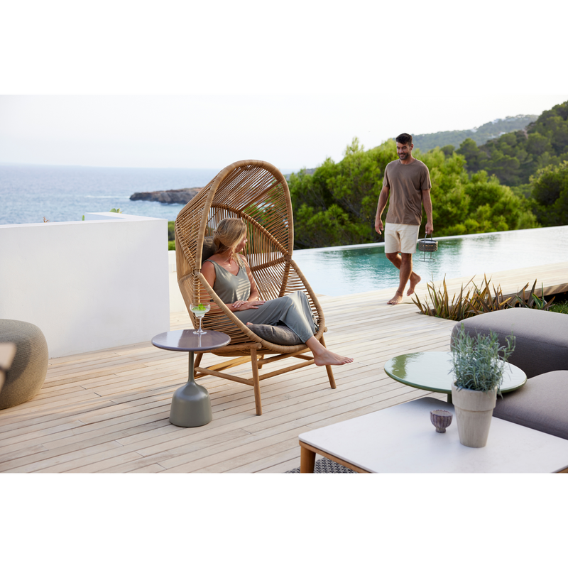 cane line hive chair Natural, small round tube Cane-line Weave with teak base and Taupe, Cane-line AirTouch cushion in a patio with a woman enjoying the chair lifestyle