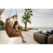 cane line hive chair Natural, small round tube Cane-line Weave and Taupe, string Cane-line Soft Rope and Taupe, Cane-line AirTouch cushion in a patio with a woman enjoying the chair lifestyle