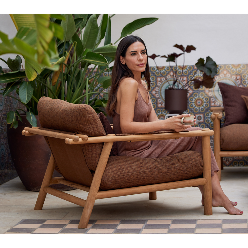 sticks lounge chair Teak Umber brown Cane-line Rise cushion with a woman enjoying the chair lifestyle