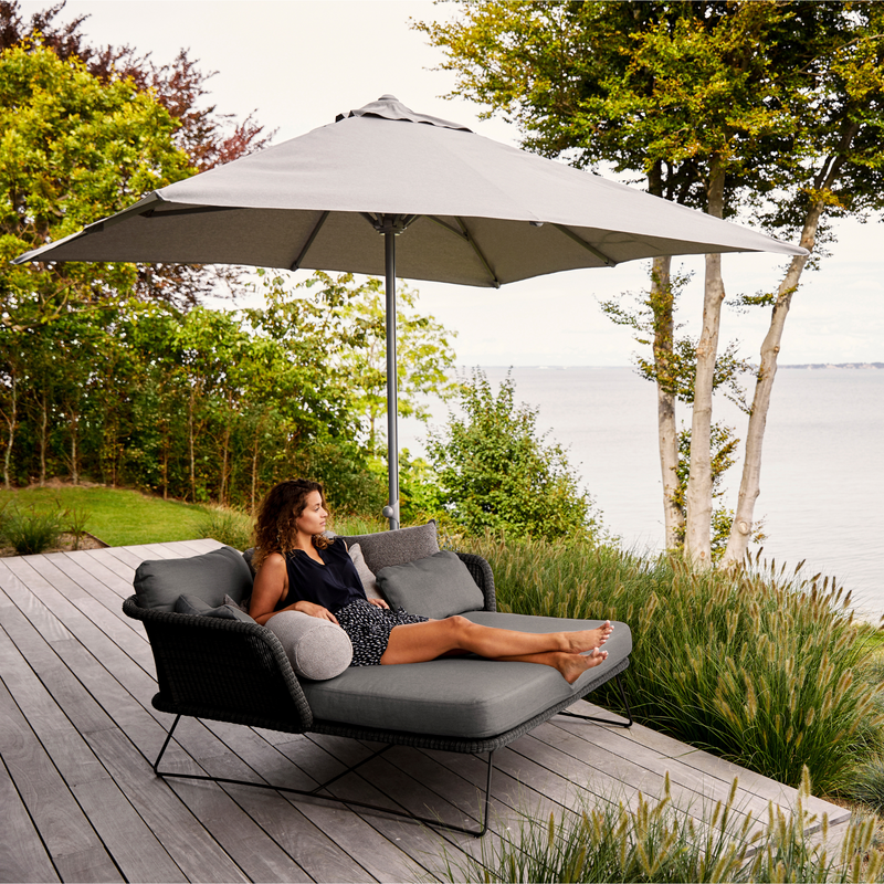 lifestyle image of cane-line horizon daybed in Black, Small Round Cane-line Weave Incl. Grey Cane-line Natté in a patio with a woman enjoying the daybed