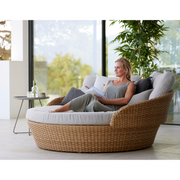 lifestyle image of cane-line ocean large daybed in Natural, Large Flat Cane-line Weave daybed with Light Brown, Cane-line Wove cushion in a patio with a woman enjoying the daybed