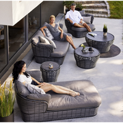 lifestyle image of cane-line basket daybed in Graphite, Braid Cane-line Weave w/Grey Cane-line AirTouch in a patio with basket furniture and a woman enjoying the daybed