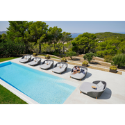 cane-line peacock daybed without parasol in a pool with all the peacock daybeds and 2 people enjoying the daybed