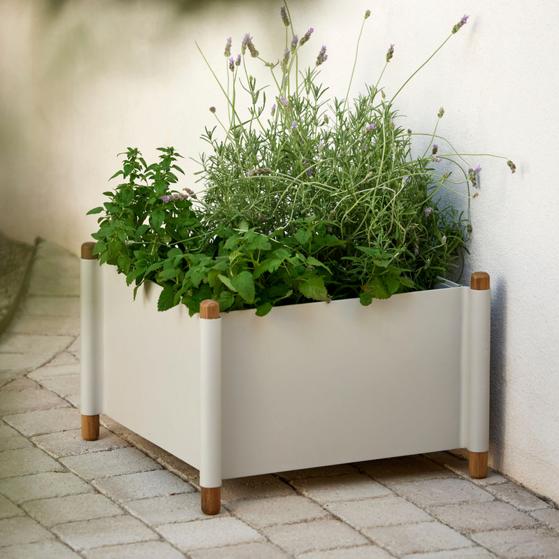 lifestyle image of cane-line sticks planter small in Teak w/Sand Aluminium with plants in a patio