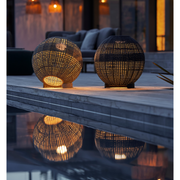 cane-line illusion lamp round taupe soft rope and dark grey soft rope lit in a patio with pool lifestyle
