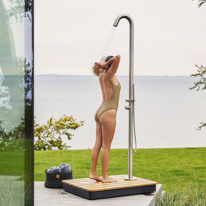 lifestyle image of cane-line lagoon shower with base in a patio and a woman enjoying the shower