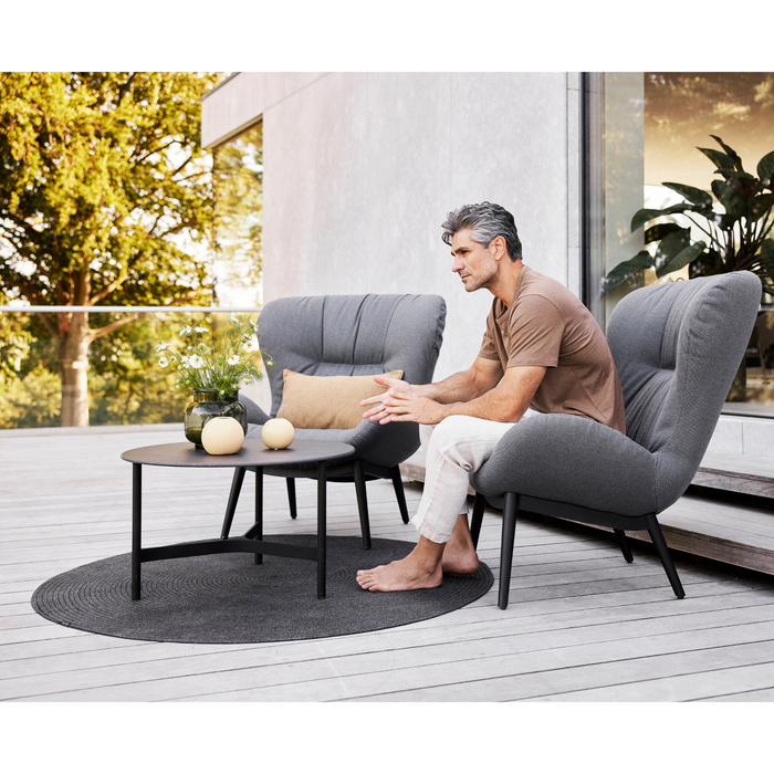 cane-line circle rug 55 dark grey soft rope in a patio with outdoor furniture and a man enjoying a chair lifestyle