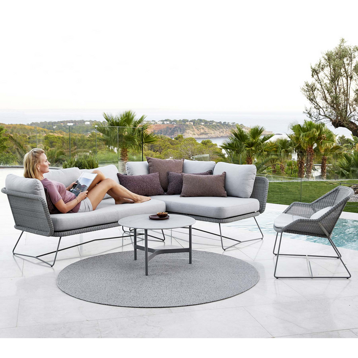 cane-line circle rug 55 taupe soft rope in a patio with pool and outdoor furniture and a woman enjoying a sofa lifestyle