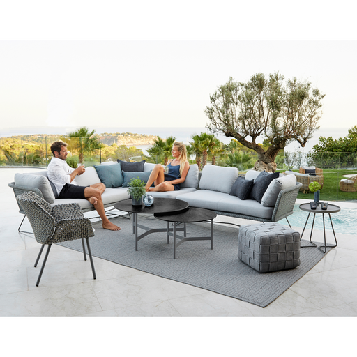 lifestyle image of cane-line cube footstool in Light Grey, Square Cane-line Soft Rope in a patio with outdoor furniture and two people enjoying a sofa