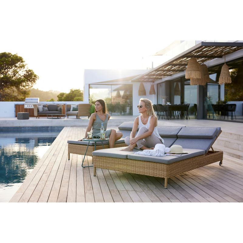 cane-line rest sunbed single Natural, large flat Cane-line Weave sunbed and Taupe, Cane-line Natté cushion in a patio with a pool and 2 women enjoying the sunbed lifestyle