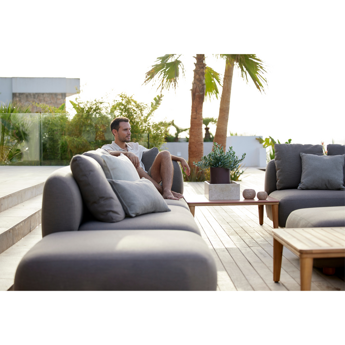 cane-line capture corner sofa with table, pouf & chaise lounge taupe, cane-line airtouch sofa in a patio with a man enjoying the sofa lifestyle