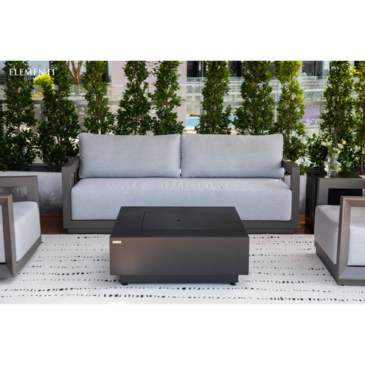 Elementi Newporrt collection Urbane Bronze Powder-Coated Frame w/ Granite Cushions Outdoor patio set , and fire pit table on a patio with plants and building in the background.