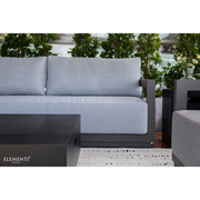 Elementi Newporrt collection Urbane Bronze Powder-Coated Frame w/ Granite Cushions outdoor sofa set with matching coffee table on a patio with greenery in the background.