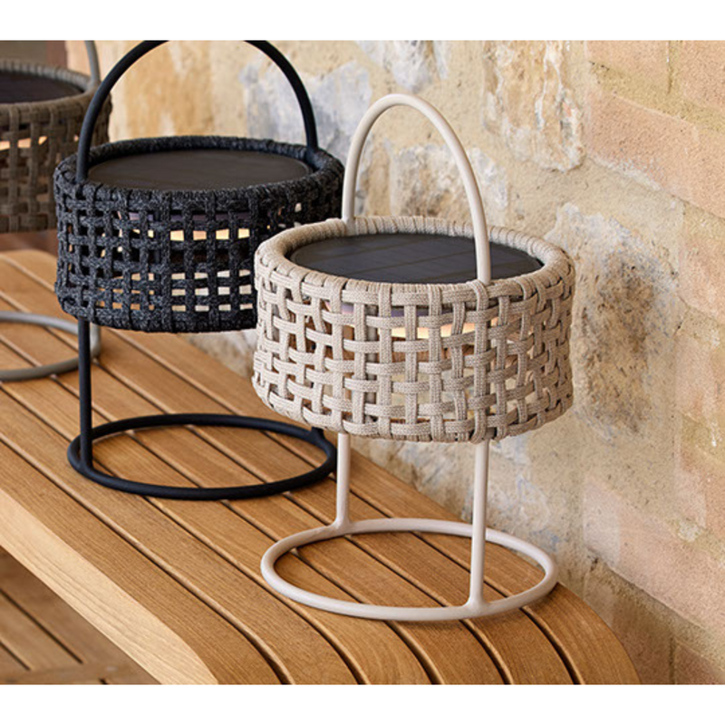 Designer outdoor furniture in multiple colors for patios and hospitality spaces. Cane-line illusion lamp solar led with sand soft rope and solar led with dark grey soft rope on mellow coffee table close up lifestyle
