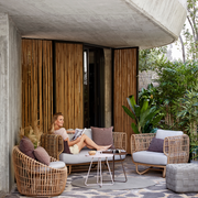 Nest outdoor 2 seater Sofa Light Grey Natte cushion in patio with outdoor furniture and a woman enjoying the sofa lifestyle