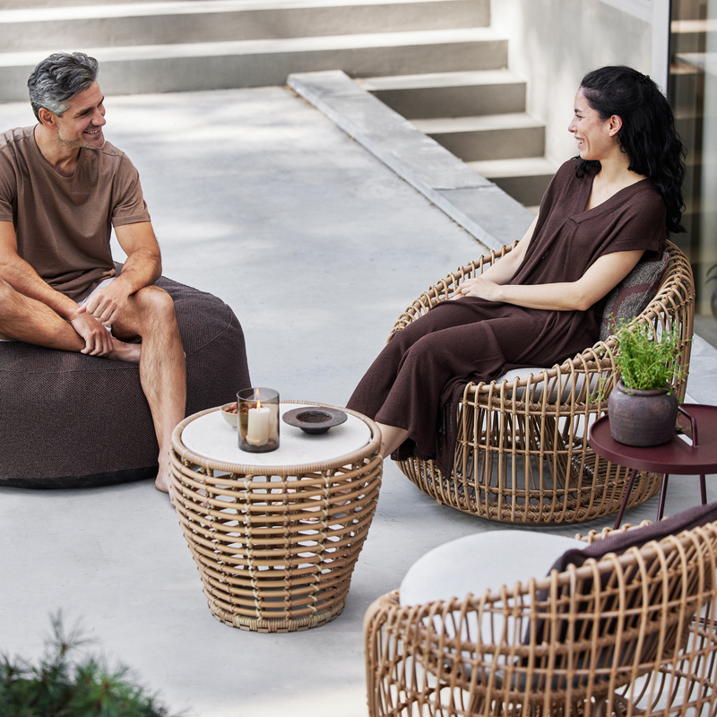 Cane line Nest outdoor round chair Natural Light Grey Natte cushion in a patio with a woman enjoying the chair lifestyle