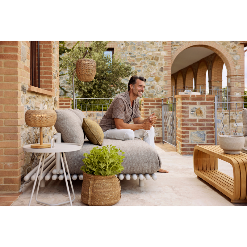 sticks platform sofa w/ chaise lounge Sand aluminium Light brown Cane-line Rise cushion in a patio with outdoor furniture and a man enjoying the sofa lifestyle