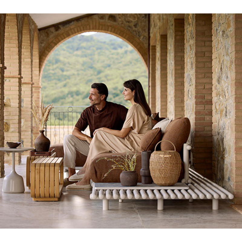 sticks platform corner sofa Sand aluminium Umber brown Cane-line Rise cushion in a patio with outdoor furniture and 2 people enjoying the sofa lifestyle