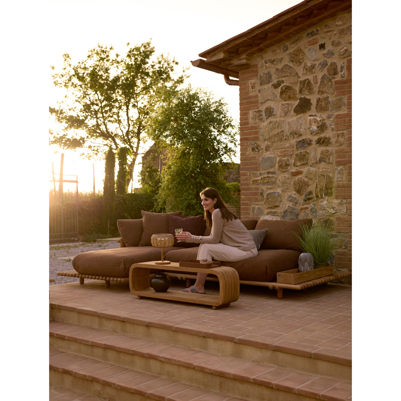 sticks platform sofa w/ chaise lounge Teak Umber brown Cane-line Rise in a patio with outdoor furniture and a woman enjoying the sofa lifestyle